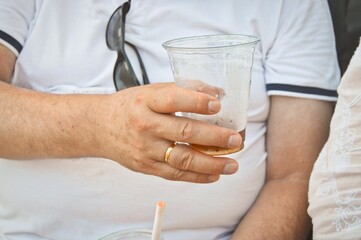Closeup shot of a male's hand with a marriage ring and a plastic cup of soda