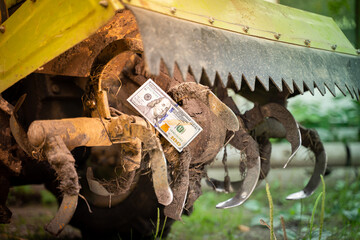 Hundred dollar bill on a dirty tractor rototiller close-up. Rotary tiller for tillage of...