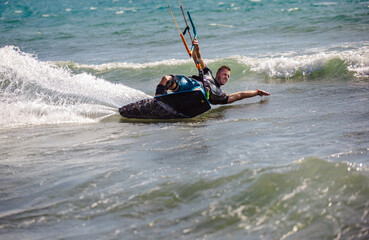 Professional kiter does the difficult trick. A male kiter rides against a beautiful background of waves and performs all sorts of maneuvers.