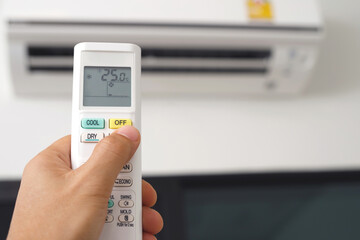Air conditioner inside the room with close up man hand holding using directed operating remote controller.