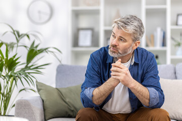 Adult mature man pensive sitting alone at home on sofa close up, gray haired person thinks looks towards window, depressed sad.