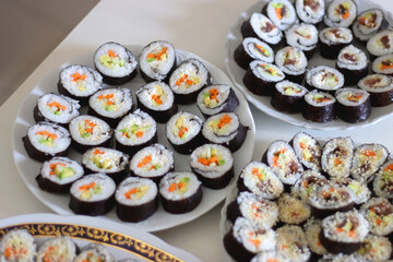 Plates with homemade sushi rolls on white table. Tuna and vegetable sushi, and vegetarian cream cheese and vegetable sushi. Selective focus.