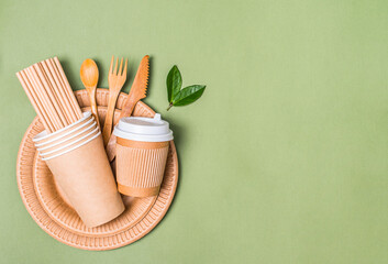 Eco-friendly tableware. Kraft paper food utensils cups plates and wooden cutlery on pastel green background with copy space. Sustainable food paper packaging.