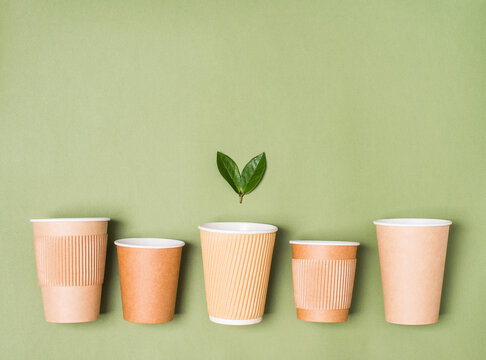 Variety Of Kraft Paper Coffee Cups With Green Leaves. Biodegradable, Compostable Paper Utensils For Hot Takeaway Beverages. Paper Cup On Green Background With Copy Space.