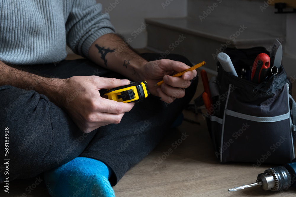 Wall mural man hands with measuring meter and pencil next to toolbox, person sitting on dining room floor