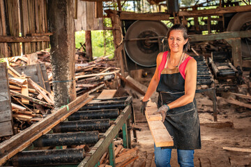 Woman smiles and winks one eye looking at camera, loading a board in a sawmill.