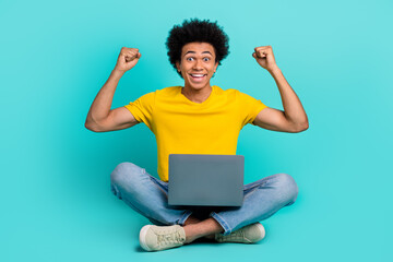 Full body photo of delighted excited person sit floor raise fists use netbook isolated on turquoise...