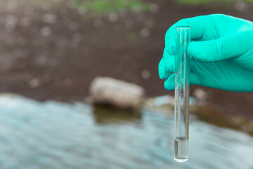 Sample water from the river for analysis. Hand in glove holding a test tube.ecology concept
