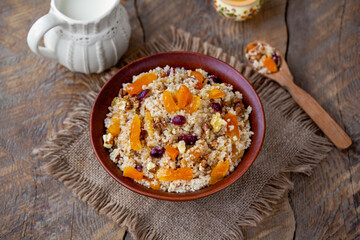 Couscous porridge. Sweet couscous with nuts and dried fruits served in a bowl with jug of milk. Wooden table, top view, selective focus, horizontal.