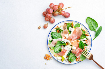 Summer pear salad with jamon, blue cheese, spinach and nuts on white table background, top view, copy space