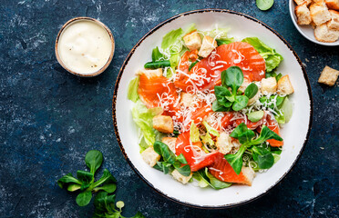 Caesar salad with salted salmon, iceberg and lamb lettuce, croutons, parmesan cheese with caesar dressing. Blue stone table background, top view