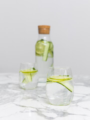 Bottle with two glasses of beauty water lemonade made of cucumber and lime standing on the white marble table