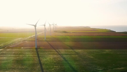 Wind turbines farm in a field. Renewable green energy. Sunny landscape electric energy generator for clean energy producing concept. Drone view in rural area. Windmills