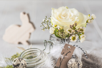 White rose and spring flowers in mason jar decorated with feathers and easter bunny