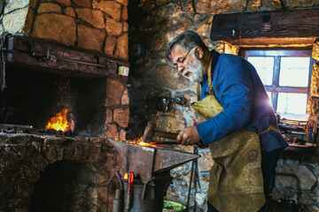 Blacksmith manually forging the molten metal on the anvil in smithy with spark fireworks