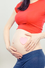 Pregnant woman showing pink heart on her belly. Expecting for newborn. Extending family