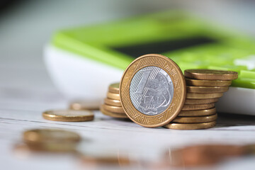 Moedas Brasileiras sobre uma mesa de madeira com uma calculadora verde na composição. Destaque...