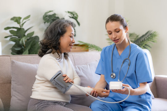 Female doctor check health and measures blood pressure of senior patient for initial examination at home.