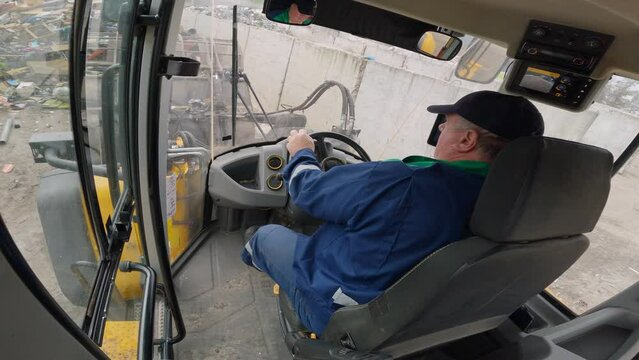 Loading a truck action and transporting waste materials with a front loader at a landfill site, inside driver cabin view. Recycling industry concept.