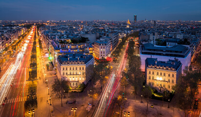 Night panorama of rooftops over Paris with old houses in the city center and light trails from cars