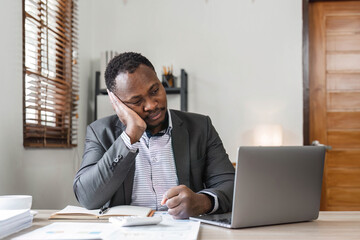 Fototapeta premium Stressed business man sitting at office workplace. Tired and overworked black man. Young african american exhausted men in stress working on laptop computer