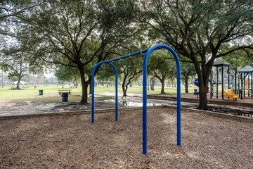 Scene of the playground with blue swing poles without swings surrounded by trees in the daytime