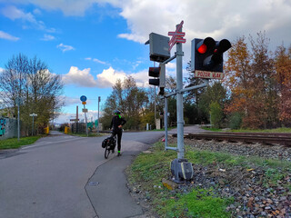 A cyclist is waiting at railway crossing with stoplights being turned on. The weather is sunny.