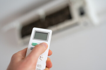 A man's hand holds a remote control from an air conditioner with a temperature on the screen of 21.