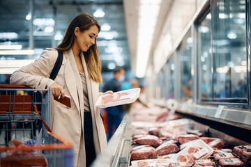 Happy woman buys meat at refrigerated section in supermarket.