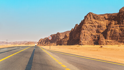 Scenic road in AlUla region of Saudi Arabia, desert with rocky formations on sides, clear sky above