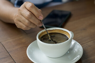 Woman hand and hot coffee in the white cup on wooden table background.Cafe drinking menu black coffee at the restaurant with copy space.