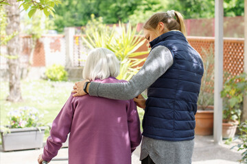 Professional young helpful caregiver walking with the elderly woman in the garden at nursing home. Elderly care concept