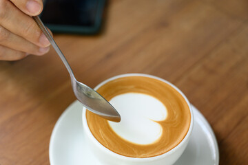 Close up woman hand and white coffee cup with heart shape latte art menu on wooden background in the cafe.