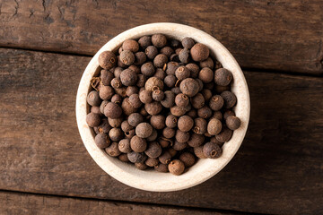 Dried allspice in bowl on wooden table. Close up. Top view