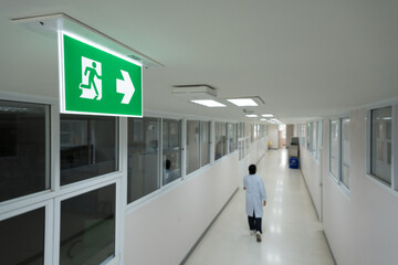 Selective fire exit sign on white ceiling.Green fire escape sign hang on the ceiling in the...