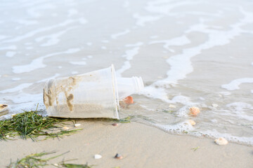 Close up plastic bottle and cup on the sand beach.Save the earth.Environment ecology care and renewable concept.Volunteer or traveller collecting plastic waste.Cleaning beach on morning time.