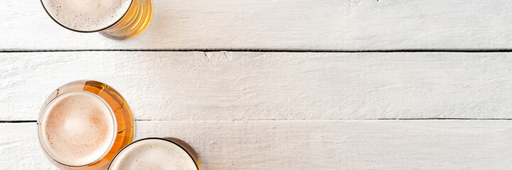 Overhead shot of beer mugs on white wooden background with copyspace