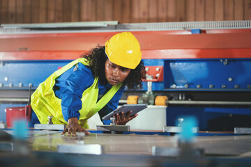 Professional african american female engineer industry worker wearing safety hard hat checking mechanic system via digital tablet in factory.