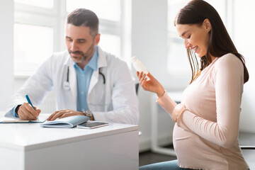 Pregnancy and medication concept. Doctor prescribing pills for young pregnant woman during...