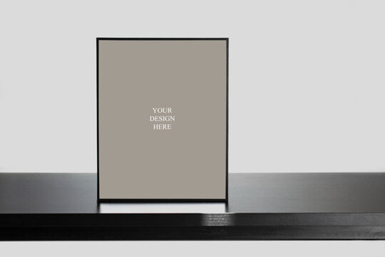 Mockup - Vertical frame standing on black wooden desk with natural shadows.