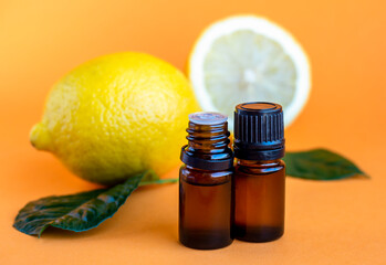 Lemon essential oil. Dark glass bottles with essential oil and lemons on orange background