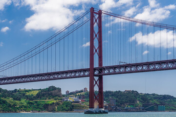 Lisbon, Portugal day sea view of Ponte 25 de Abril Suspesnion Bridge against blue sky with clouds over the Tagus River.