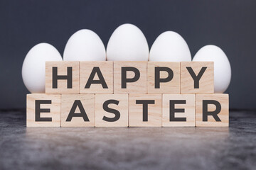 Happy Easter on wooden cubes, in front of white eggs standing on a stone background.