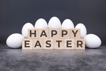 Happy Easter on wooden cubes, in front of white eggs standing and lying on a stone background....