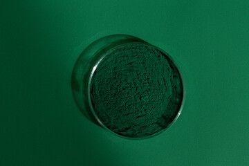 Fresh spirulina algae powder on a green background, in a petri dish, on a green background, organic spirulina powder