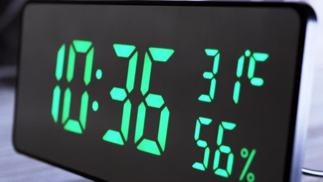 Digital Clock Showing Time on Green Display 10:36 AM, Temperature, Air Humidity. Modern mirror clock, alarm clock with a thermometer, hydrometer standing on a desk on white background. Time concept.