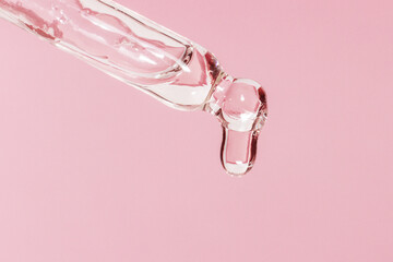 Cosmetic pipette with dripping liquid and drops on a pink background, serum, serum, gel, vitamin, water, oil
