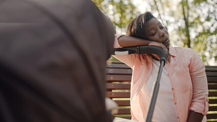 Exhausted black mother napping, leaning head on baby stroller, lack of sleep