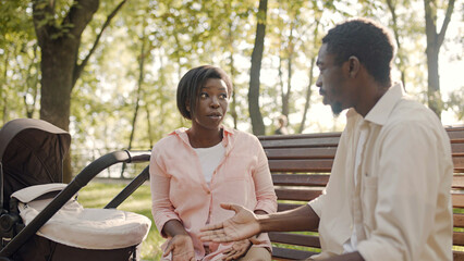 Young black parents arguing about parenting duties, sitting on bench in park