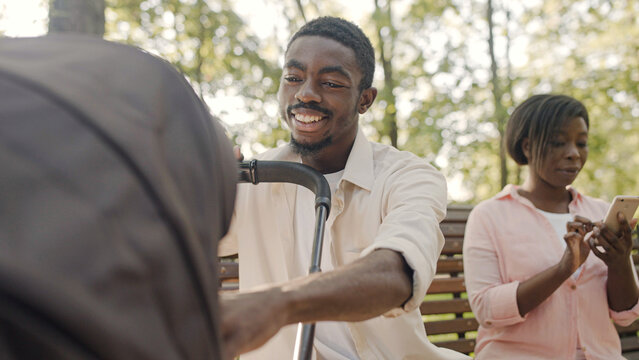 Caring father admiring newborn child while mom is using smartphone, family in park